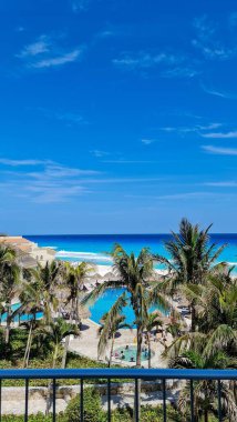 Bereketli palmiye ağaçları, açık mavi bir havuz ve güneşli bir gökyüzü altında kristal okyanus dalgalarının yer aldığı büyüleyici bir tropikal cennet manzarası. Mükemmel plaj günü.