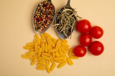 Pişmemiş makarna, vişneli domates, biber ve bej arka planda kuru otlar. Üst manzara, yemek kompozisyonu.