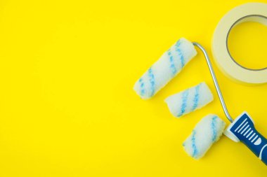 Parlak sarı bir zemin üzerine yerleştirilmiş birden fazla başlıklı ve maske bantlı düz bir boya silindiri. Metin veya tasarım yerleştirme için sol tarafında büyük boş alan olan minimalist yerleşim.