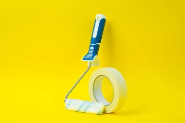 Sarı arkaplan üzerinde dikey duran boya silindiri ve bant, kopyalama alanı ile ortalanmış kompozisyon