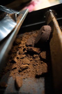 Ticari espresso makinesi çekmecesinde kullanılmış kahve telvesi yakın plan. Koyu, desenli kahve paketleri ve metalik yüzeye yayılmış gevşek çimenler..