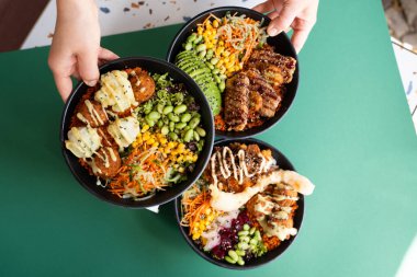 Üç kase falafel, avokado, sebze ve ızgara et, üst manzara, el ele tutuşmalar, yeşil arka planda izole edilmiş..