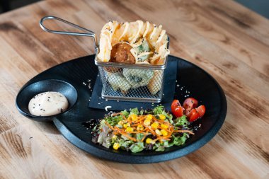 Soslu çıtır waffle kızartması ve siyah tabakta taze salata. Üst manzara, ahşap masada izole edilmiş..