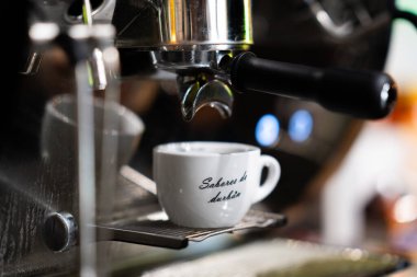 Kahve makinesinden beyaz fincana akan Espresso, yakın çekim, ön görüş, kafenin içinde izole edilmiş..