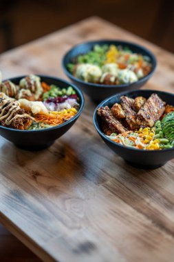 Çeşitli malzemelerle dolu üç kase, ön manzara, ahşap masa arkasında izole edilmiş..