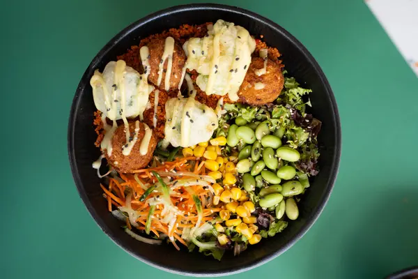 Mısır, edamame, yeşillik ve kremalı soslu falafel poke kasesi, üst manzara, yeşil arka planda izole edilmiş..