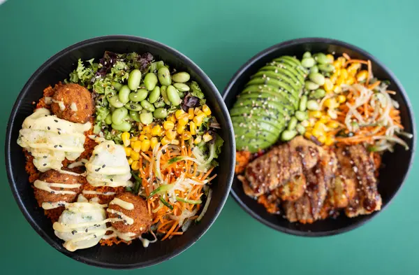 Falafel, avokado, ızgara et ve sebzelerle dolu iki kase, yeşil arka planda izole edilmiş..