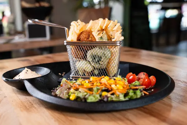 Karışık sebzeli waffle kızartması ve siyah tabakta sos, ön manzara, ahşap masada izole edilmiş..