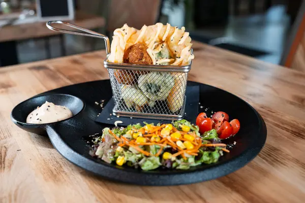 Soslu bir sepet waffle kızartması ve siyah tabakta taze sebze salatası.