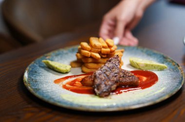 Kızarmış biftek, patates kızartması ve soslu restoran tabağı.