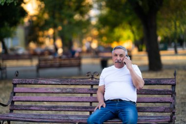 Park Bench 'te otururken telefonda konuşan kıdemli adam.