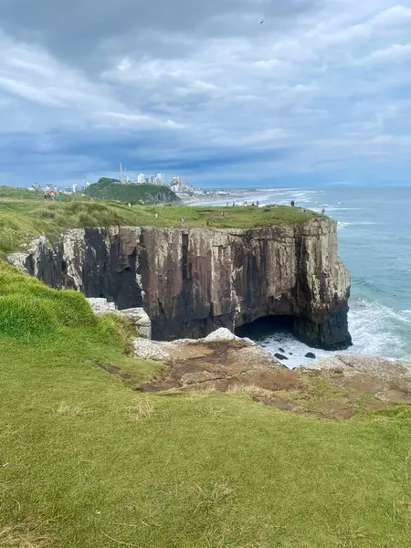 Uçurumun kenarından çarpıcı bir manzara. Denize doğru eğilmiş dramatik kaya oluşumları. İnsanlar yemyeşil çimenlerin manzarasının tadını çıkarırken gökyüzü gri bulutlarla dolu..