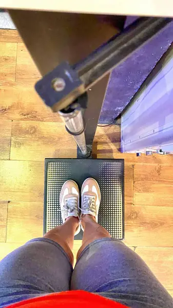 Dijital ölçekte duran birinin yukarıdan çekilmiş bir görüntüsü. Modern, açık renkli spor ayakkabılar giyiyorlar ve kırmızı şort ve gömlek giyiyorlar. Ahşap zemin ve arkaplan çağdaş bir ayarı vurgular, davet edici bir refleks