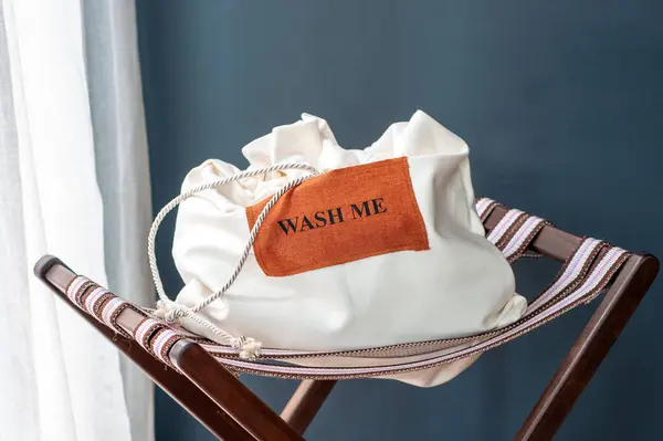 Sandalyede beyaz çamaşır torbası, arka planda koyu renk, mesajla yıka beni..