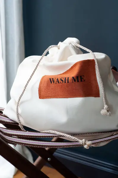Sandalyede beyaz çamaşır torbası, arka planda koyu renk, mesajla yıka beni..