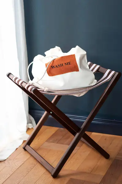 Sandalyede beyaz çamaşır torbası, arka planda koyu renk, mesajla yıka beni..