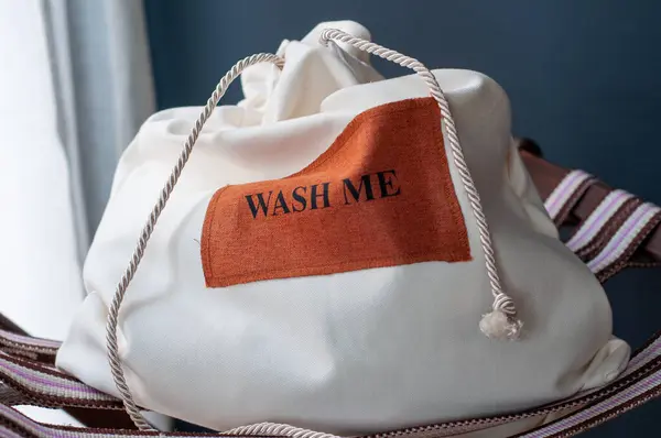 Sandalyede beyaz çamaşır torbası, arka planda koyu renk, mesajla yıka beni..
