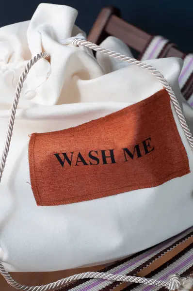 Sandalyede beyaz çamaşır torbası, arka planda koyu renk, mesajla yıka beni.