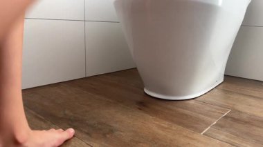 Küçük kız tuvalette oturur ve bacaklarını sallar, sadece ayakları ve bacakları görünür.. 