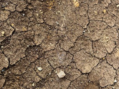 Çatlamış sert bir yüzey, düzensiz dokuları ve doğal erozyon çizgileri olan kuru toprak, kurak araziyi betimliyor..