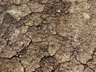 Çatlamış sert bir yüzey, düzensiz dokuları ve doğal erozyon çizgileri olan kuru toprak, kurak araziyi betimliyor..