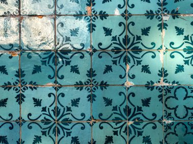 Simetrik çiçek desenleri ve gözle görülür aşınma ve yüzey değişimine sahip parlak gök mavisi seramik fayanslardan oluşan fayanslardan oluşan fayanslı bir duvar..