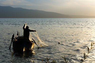Gölde balıkçı ağıyla çalışan balıkçı silueti.