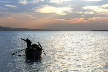Balıkçı silueti ve balıkçı ağıyla çalışan bir tekne.