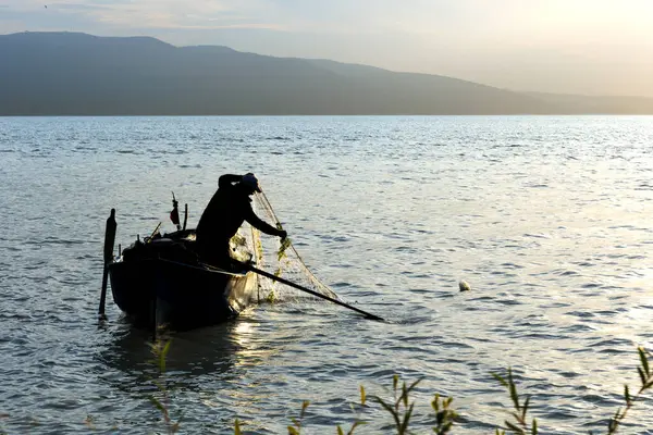 Gölde balıkçı ağıyla çalışan balıkçı silueti.