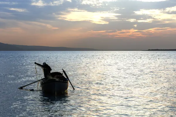 Balıkçı silueti ve balıkçı ağıyla çalışan bir tekne.