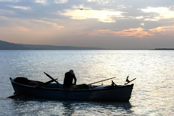 Balıkçı silueti ve balıkçı ağıyla çalışan bir tekne.