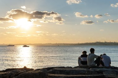 İnsanlar kayanın üzerinde oturup güneşin tadını çıkarıyorlar.