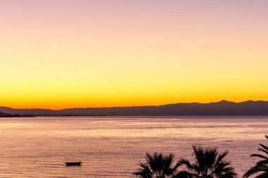 silhouette of a boat and sunrise on the  Agean sea with palm trees and boat in the foreground,from Edremit, Balkesir