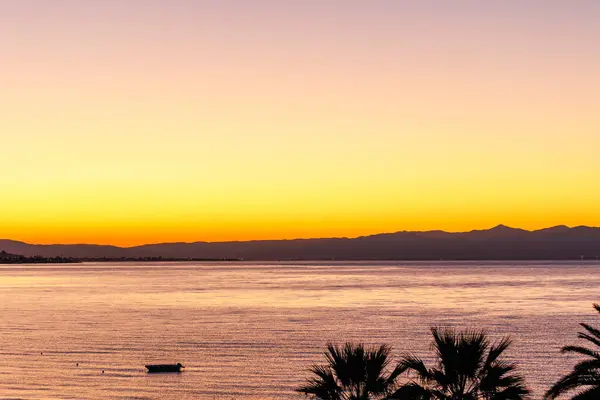 silhouette of a boat and sunrise on the  Agean sea with palm trees and boat in the foreground,from Edremit, Balkesir