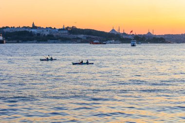 İnsanlar İstanbul 'un batımında ve şehrinde tarihi yarımadası olan boğazda kürek çekiyorlar.