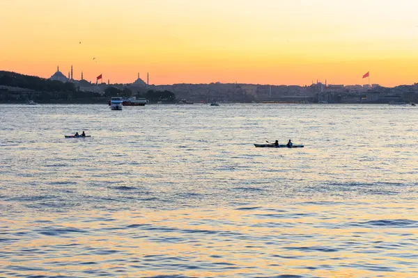 İnsanlar gün batımında İstanbul 'un batımında ve şehir merkezinde Süleyman Camii ile birlikte kürek çekiyorlar.