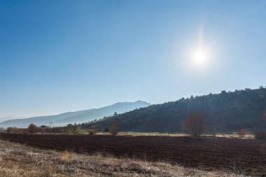 Sisli bir sabahta, Konya 'da mavi gökyüzünün altındaki tarlalar ve çiftliklerle dağların manzarası.