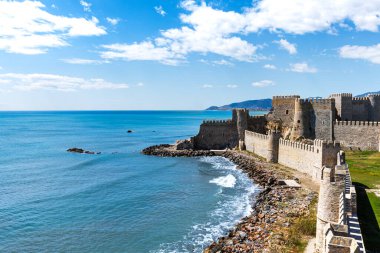 Akdeniz kıyısının güzel manzarası ve mavi bulutlu gökyüzünün altında bir kale duvarı.