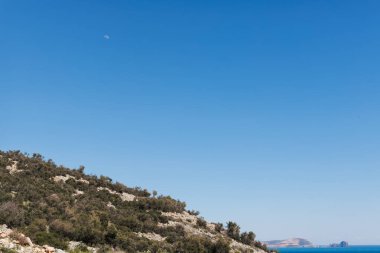 Öğleden sonra dağların üzerinden mavi gökyüzünde yarım ay.