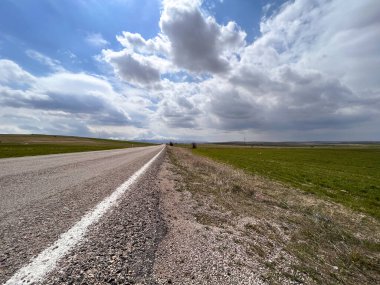 Parçalı bulutlu bir günde kırsal kesimdeki bir çiftlik arazisinin yakınında boş bir asfalt yol.