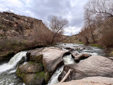 Vadideki kayaların arasından akan nehir suyu bulutlu bir günde dağların arasına düşüyor.