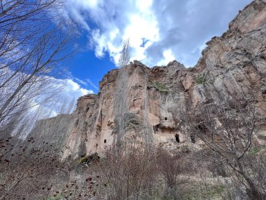 Bulutlu mavi bir gökyüzünde dağın tepesinde oyulmuş bir mağara.
