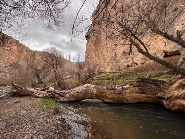Bulutlu bir günde vadide akan nehirde, dağların arasında tahta bir köprü.