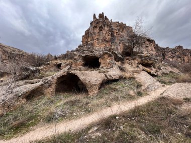 ilginç jeolojik oluşumu olan mağaraların yakınında kirli bir patika ve bulutlu bir günde kayalık bir tepe.