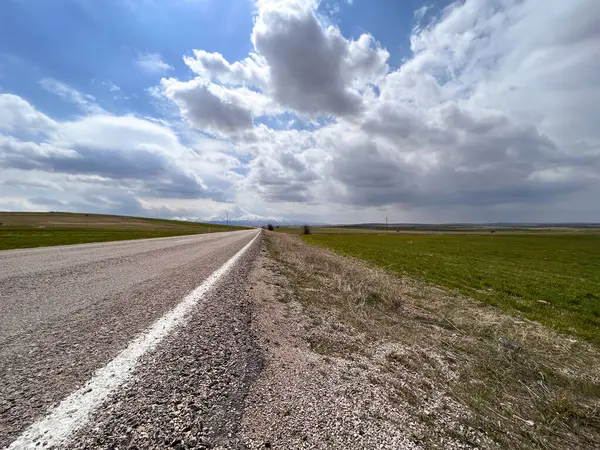 Parçalı bulutlu bir günde kırsal kesimdeki bir çiftlik arazisinin yakınında boş bir asfalt yol.