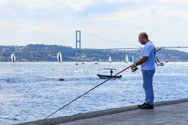a fisher man is catching fish on the coastline of Bosphorus while 24th Bosphorus Cup is running on 20 September 2025