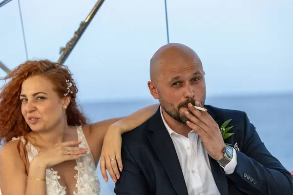 Gelin beyaz gelinlik içinde ve damat deniz zemininde sigara içiyor.