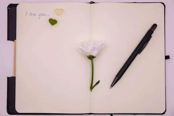 Beyaz arka planda çiçekli kalem ve defter, seni seviyorum mesajı, sevgililer günü konsepti