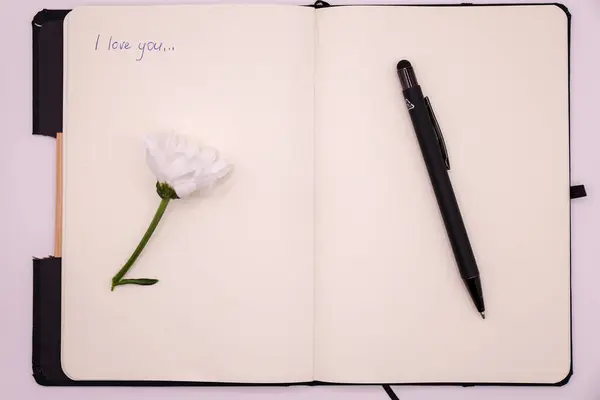 Beyaz arka planda kalem ve beyaz çiçekli defter. Mesajını seviyorum, üst görünüm.