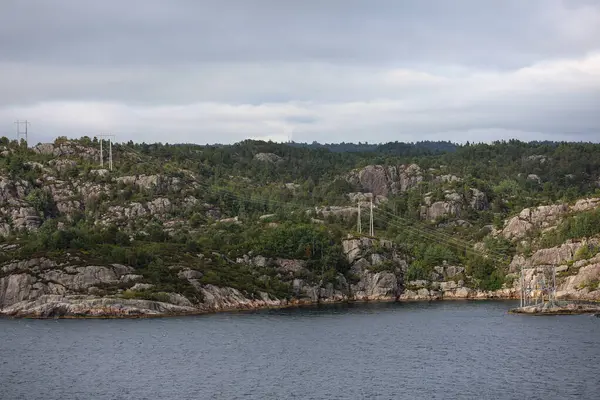 Yazın Norveç fiyordunun kayalık kıyıları. Kayalık dağlardaki elektrik hatları